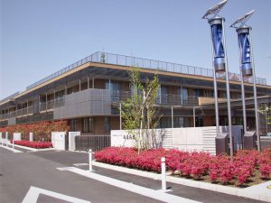 介護施設の建物外観。駐車場側から見た全景、ピンク色の花壇が配置される